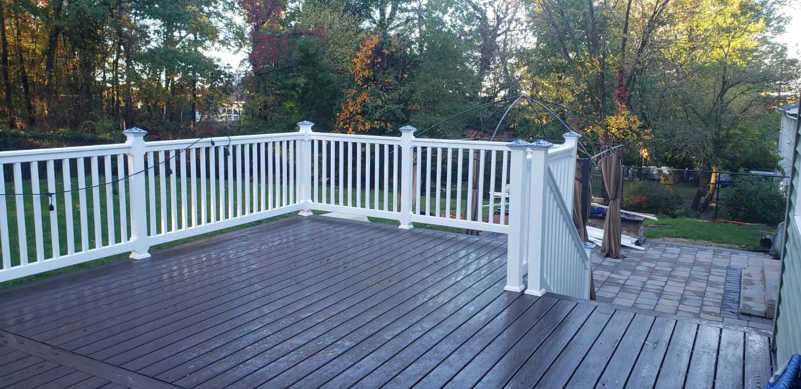 Completed composite deck with white railings overlooking a wooded yard.